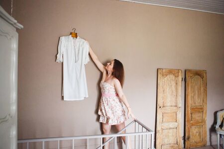 Provence. Girl takes off white dress from the wall in the bedroom.の写真素材