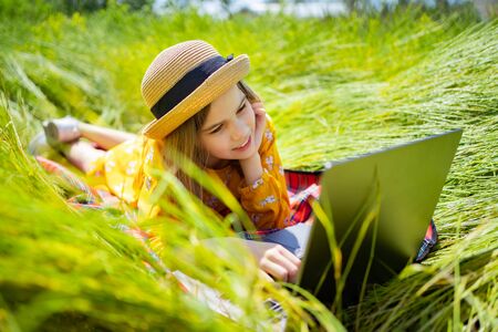 little girl learns, a teenager working on laptop lying on a meadow. mobile Internet in rural areas....