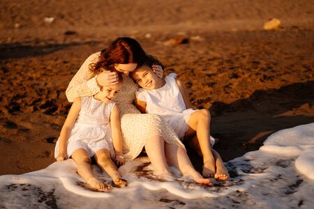 mother with daughters sitting on the sand, on the beach by the sea. the relationship of parents with children. family vacation.の写真素材