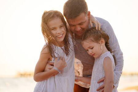 dad wipes and warms daughters after swimming in the sea in dresses. children in wet clothes. the holiday with kids. father day.の写真素材