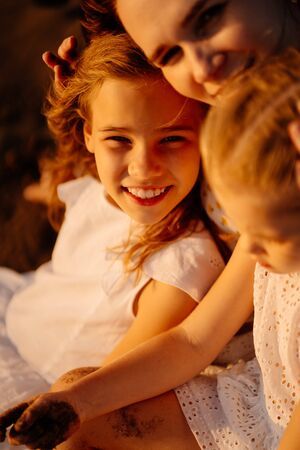 mother with daughters sitting on the sand, on the beach by the sea. the relationship of parents with children. family vacation.の写真素材