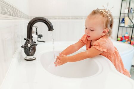 baby girl in crown on his head, washes his hands in the bathroom. hygiene and cleanliness. disease prevention.の写真素材