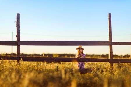 at sunset child, girl in the hat standing next to a fence in the village. walks in the countryside....