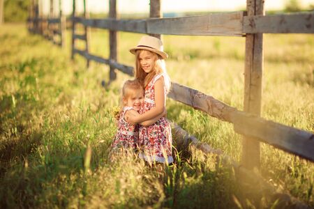 children, girls in the hat standing next to a fence in the village. walks in the countryside. farming.の写真素材