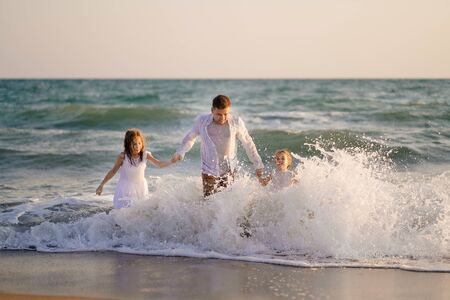 wet dad and daughters swimming in the sea in clothes, playing and having fun together on the beach. family vacation. father day.の写真素材