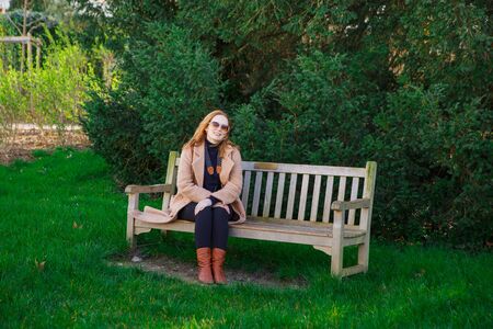 girl in coat sitting on a bench in spring Park. walks in the outdoors.の写真素材