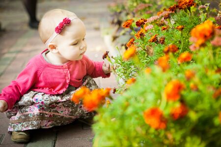 little girl with short hair in a dress sitting on the street near the flower beds. walks in the outdoors.の写真素材