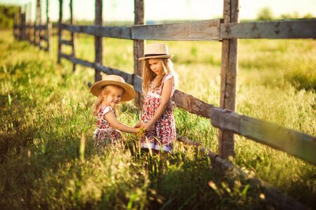 children, girls in the hat standing next to a fence in the village. walks in the countryside. farming.の写真素材