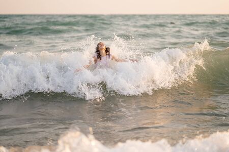 teenager girl in a dress swims in the sea with high waves. entertainment in the vacation. trips with children.の写真素材
