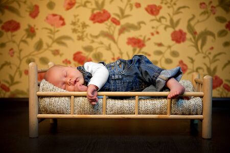 babe in denim overalls sleeps in a little cot toy. care for newborn children.の写真素材
