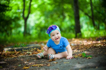 little girl in blue dress and headband with flowers sitting on the ground in the Park. a walk with the kids.の写真素材