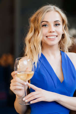 beautiful blonde girl with long hair in a blue dress standing with a glass of wine. a romantic dinner.の写真素材