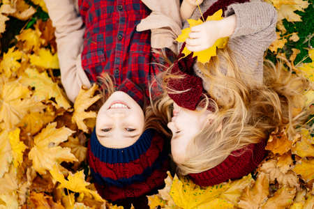 two little girls in the hat lying on the ground on yellow maple leaves in autumn Park