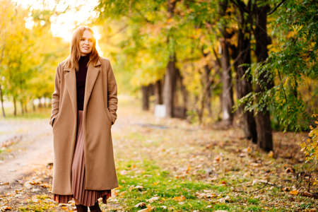 the setting sun. calm woman in coat standing on a footpath in autumn Park. nature walks.の写真素材