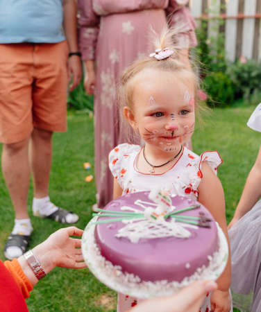 little girl with face paint eating birthday cake on the lawn at the festival.の写真素材