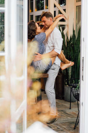 the view through the door from the street to the couple hugging near the wooden table. romantic relationship.の写真素材