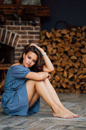 beautiful brunette girl in blue dress sitting barefoot on the floor in a country house.の写真素材