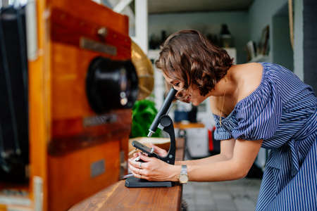 beautiful brunette girl looks into an ancient microscope. collecting vintage items.