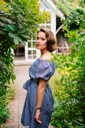 beautiful brunette girl in blue dress walking in the summer garden in the backyard of a country house.の写真素材