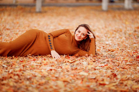 a beautiful pregnant woman lies on fallen dry leaves in an autumn Park.