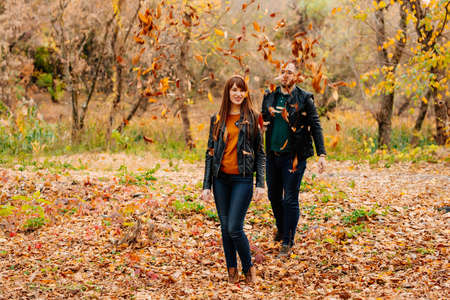 a man showers dry leaves on a woman in an autumn park. romantic walk.の写真素材