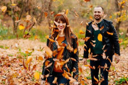 a man showers dry leaves on a woman in an autumn park. romantic walk.