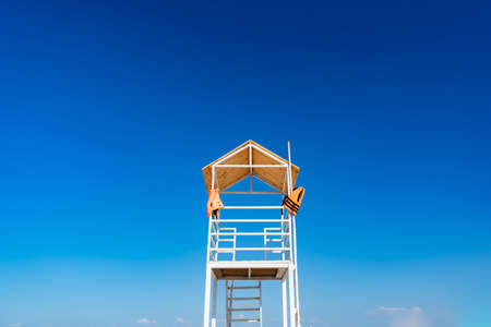 a white wooden lifeboat tower on the beach against a clear blue sky. concept of water safety and tourism.の写真素材