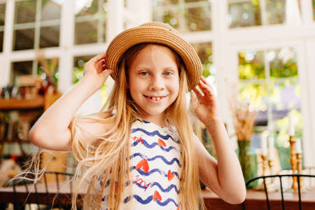 close up. a cute girl in a straw hat with long hair and a dress is standing in a vintage-style room....