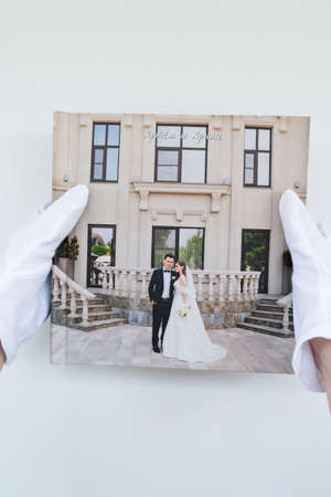 hands in white gloves holding a photo book with wedding photos. beautiful and convenient storage of the memory of an important day. Russian names Artyom and Arina are written on the cover.の写真素材