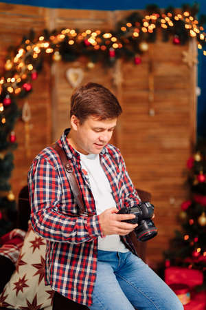 male photographer in a plaid shirt with a camera at the Christmas tree. traditional New year family photo sessions in the Studio. seasonal work. festive atmosphere.の写真素材