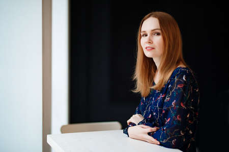 a woman with red hair in a blue dress is sitting at a table. reception worker in the office.