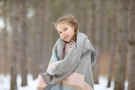 a little girl wrapped in a scarf in a snowy winter forest. travel and recreation with children in winter. walking in the fresh air during the new year holidays.の写真素材