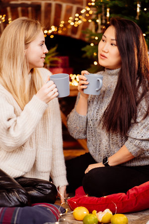 Two woman drinking tea by fireplace with New Years decoration. Romantic.の写真素材