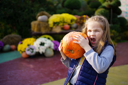 Funny girl writhes faces with pumpkin in hands on walk in park on Halloween.の写真素材