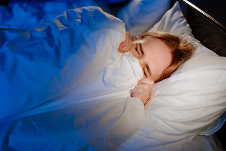 a woman lies in bed under a white blanket and afraid, frightened.の写真素材