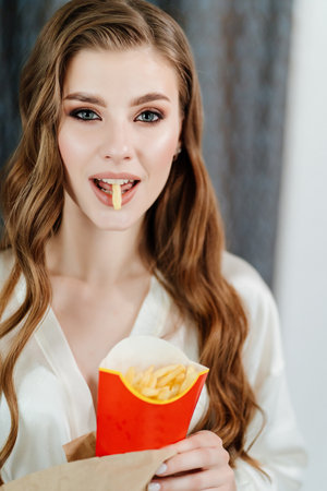 beautiful young woman with long hair and makeup eating French fries.