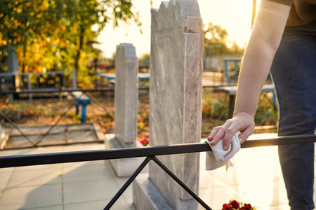 Cleaning cemetery. A womans hand washes black fence at grave with rag.の写真素材