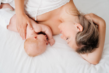 mom is mom is lying down with a baby in a white bed after feeding breast milk.の写真素材