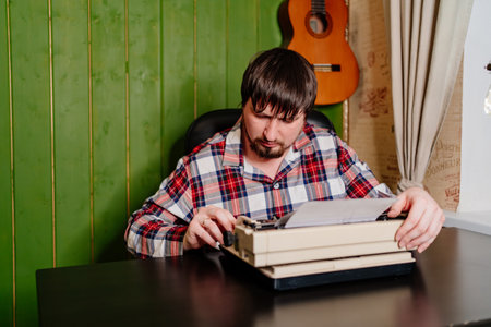 a man in plaid pajamas types on a typewriter at night in his home office.