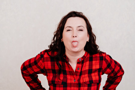 A brunette woman in a red dress on a white background shows off her tongue.の写真素材