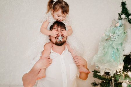 daughter sits on shoulders of father and hangs toy star on nose instead of treeの写真素材