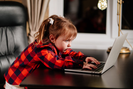 a little girl imitates her mother and works on a computer at home in evening.の写真素材