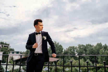 a young man in a black jacket with a bud of flowers stands on the balcony. groomの写真素材