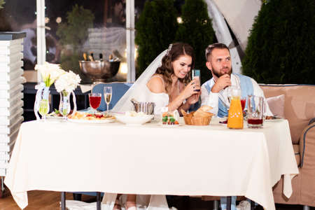 newlyweds sit at table in restaurant and listen to congratulations from guests.の写真素材