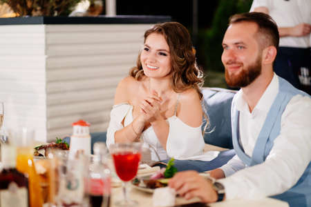 newlyweds sit at table in restaurant and listen to congratulations from guests.の写真素材