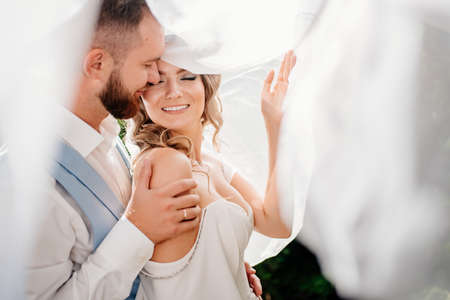 under the veil Happy and beautiful bride and groom gently cuddle in the parkの写真素材