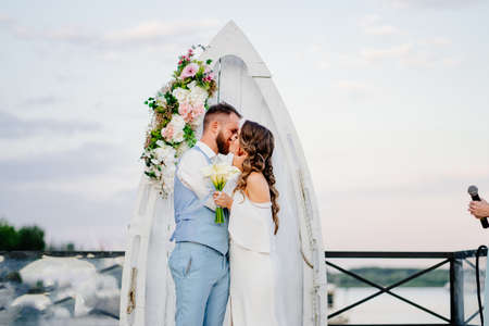 happy newlyweds kiss. beautiful wedding ceremony by water on dock.の写真素材