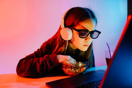 girl in glasses 3D and headphones carefully watches movie on laptop,eats popcorn