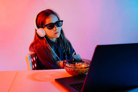 girl in glasses 3D and headphones watches boring movie on laptop, eats popcornの写真素材