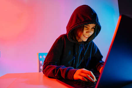 A girl in dark hooded clothes works at night at the computer